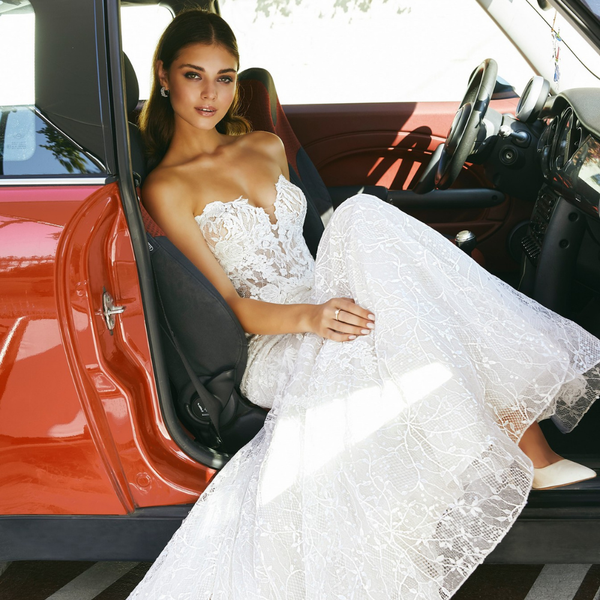 Thumbnail of model sat in a red Mini in Ronald Joyce style 69707, a strapless lace fit and flare wedding dress with a feminine sweetheart neckline and illusion bodice 